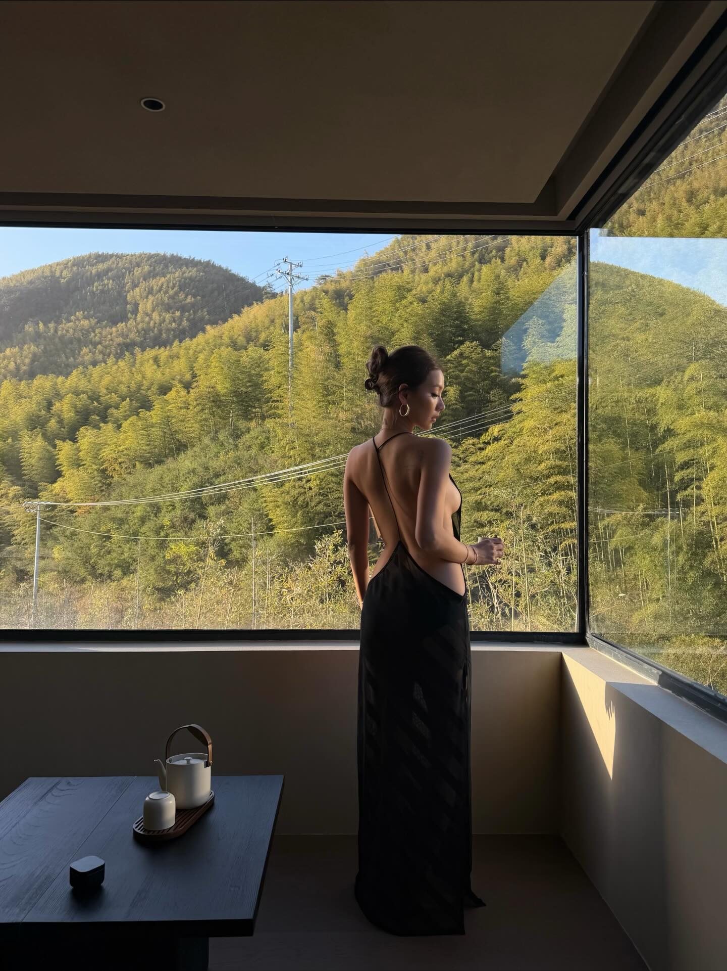 Kathy Zheng in a backless black dress at a window facing bamboo hills