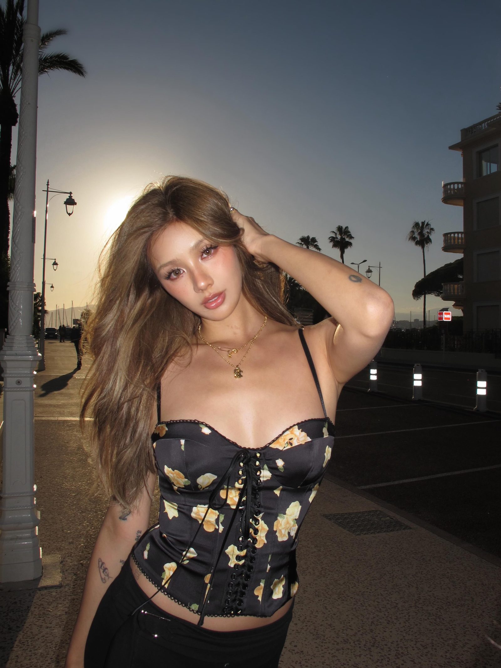Kathy Zheng in a floral corset top on a palm-lined promenade at sunset