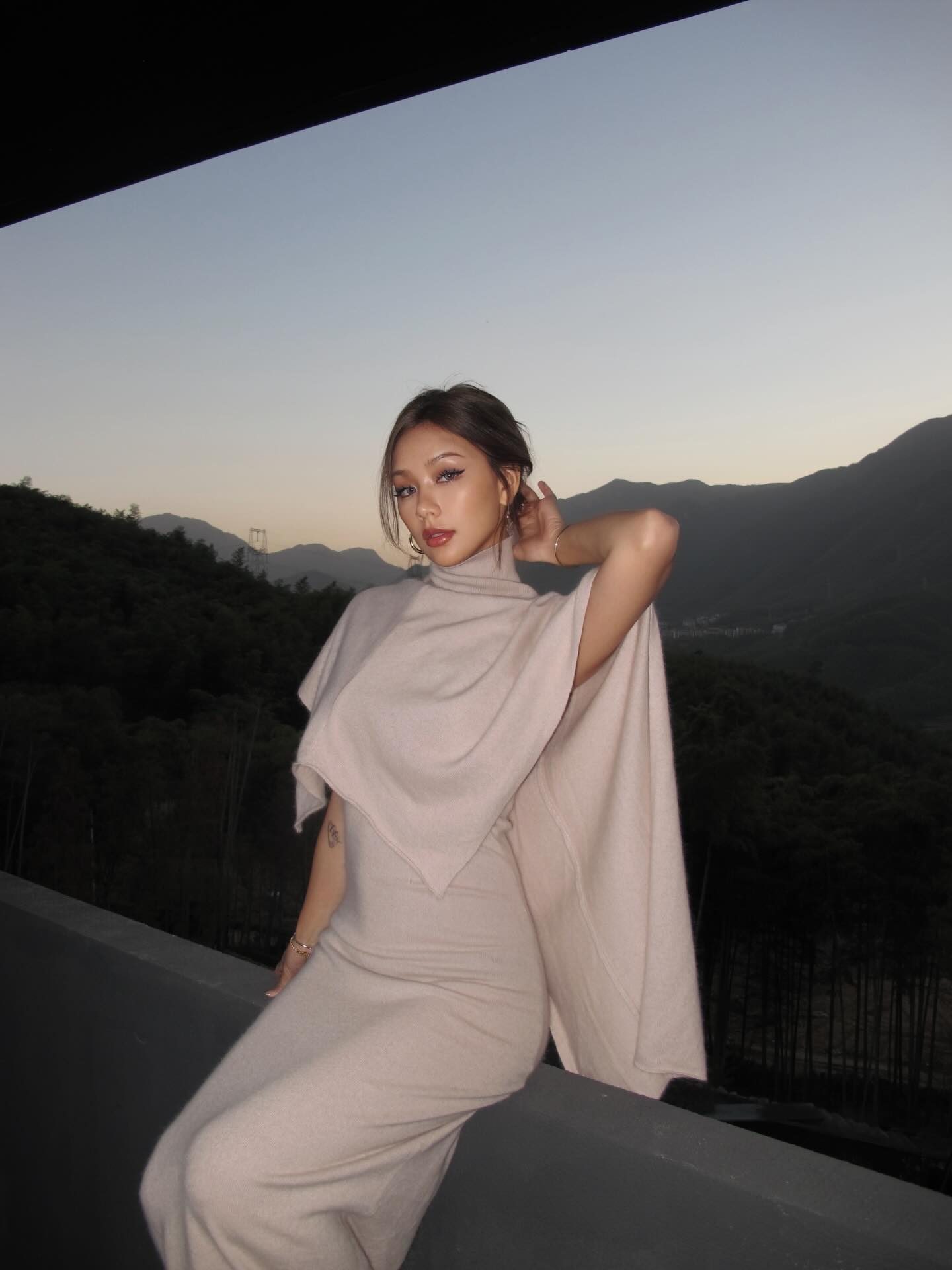 Kathy Zheng in a blush cashmere cape on a terrace at dusk