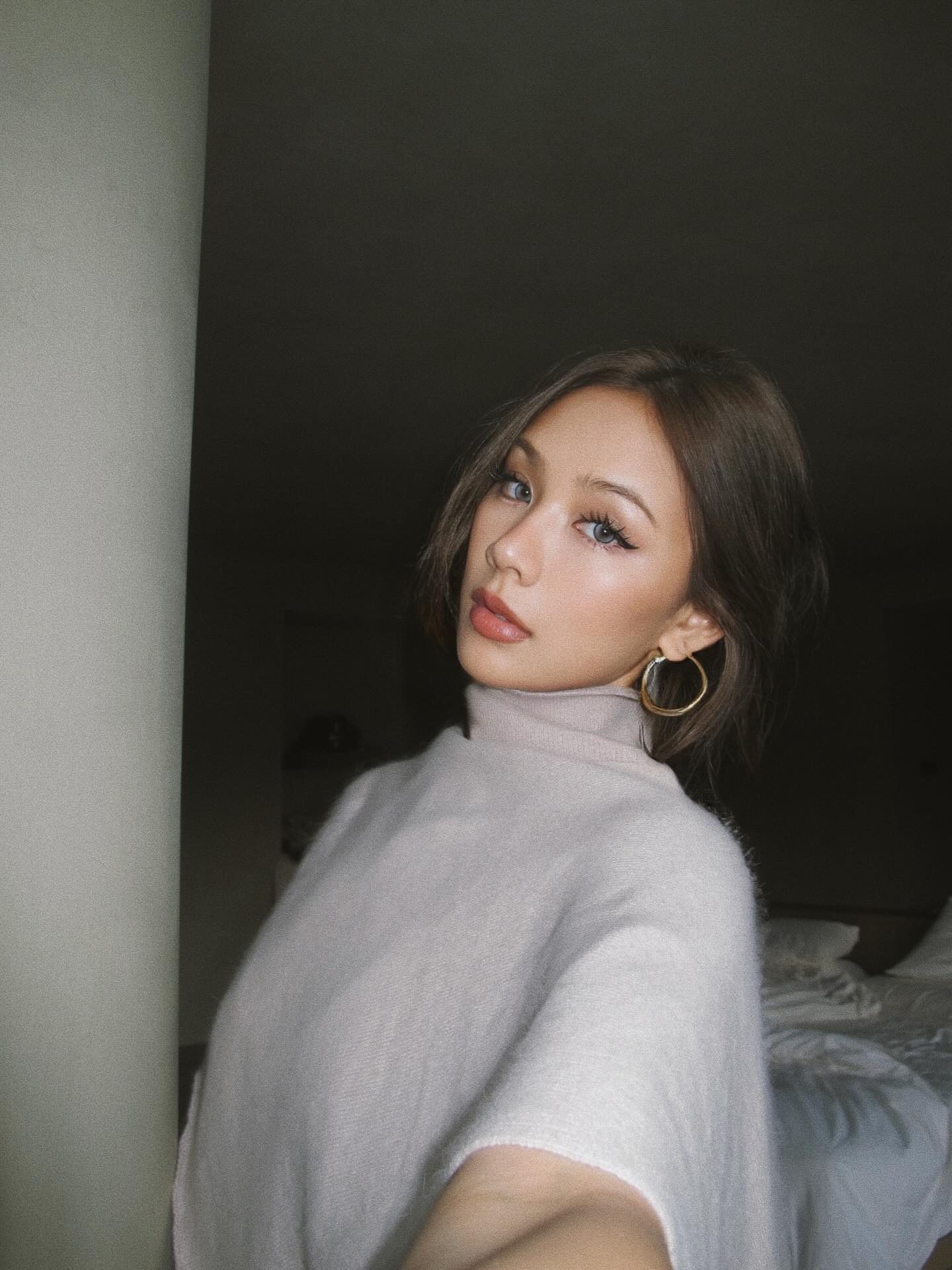 Kathy Zheng in a soft grey turtleneck with gold hoop earrings