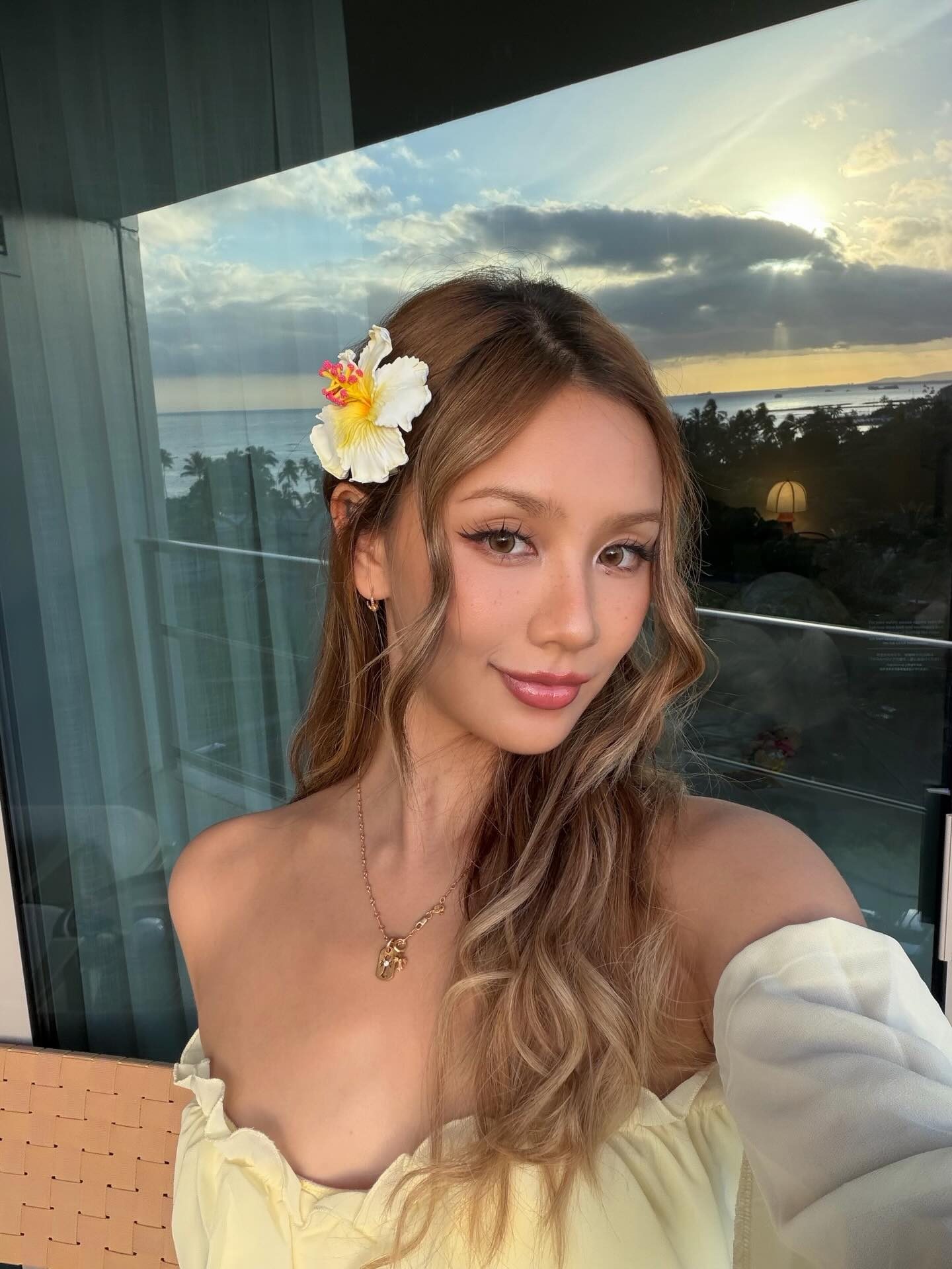 Kathy Zheng with a white hibiscus in her hair on a balcony at sunset