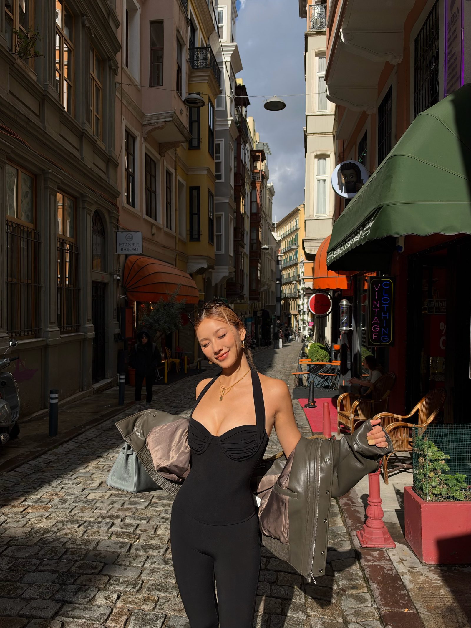 Kathy Zheng smiling on a cobblestone street, leather jacket off her shoulders