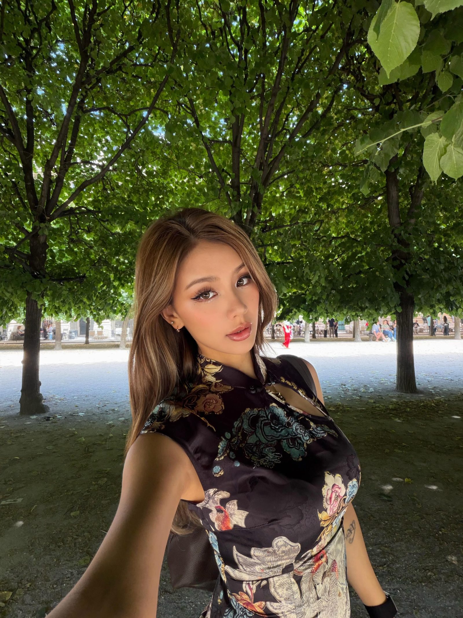 Kathy Zheng in a black brocade qipao beneath a canopy of trees