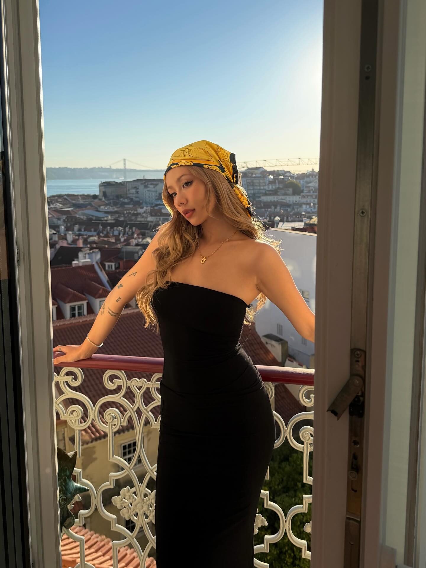 Kathy Zheng in a black strapless dress and yellow silk scarf on a balcony over Lisbon