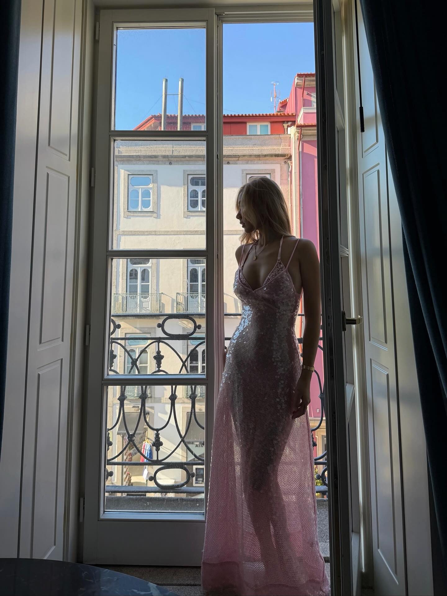 Kathy Zheng silhouetted in a pink sequin gown at a tall balcony window