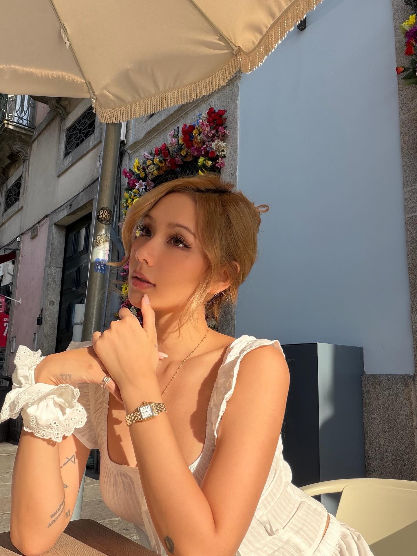 Kathy Zheng in white, chin on hand, beneath a fringed cafe parasol