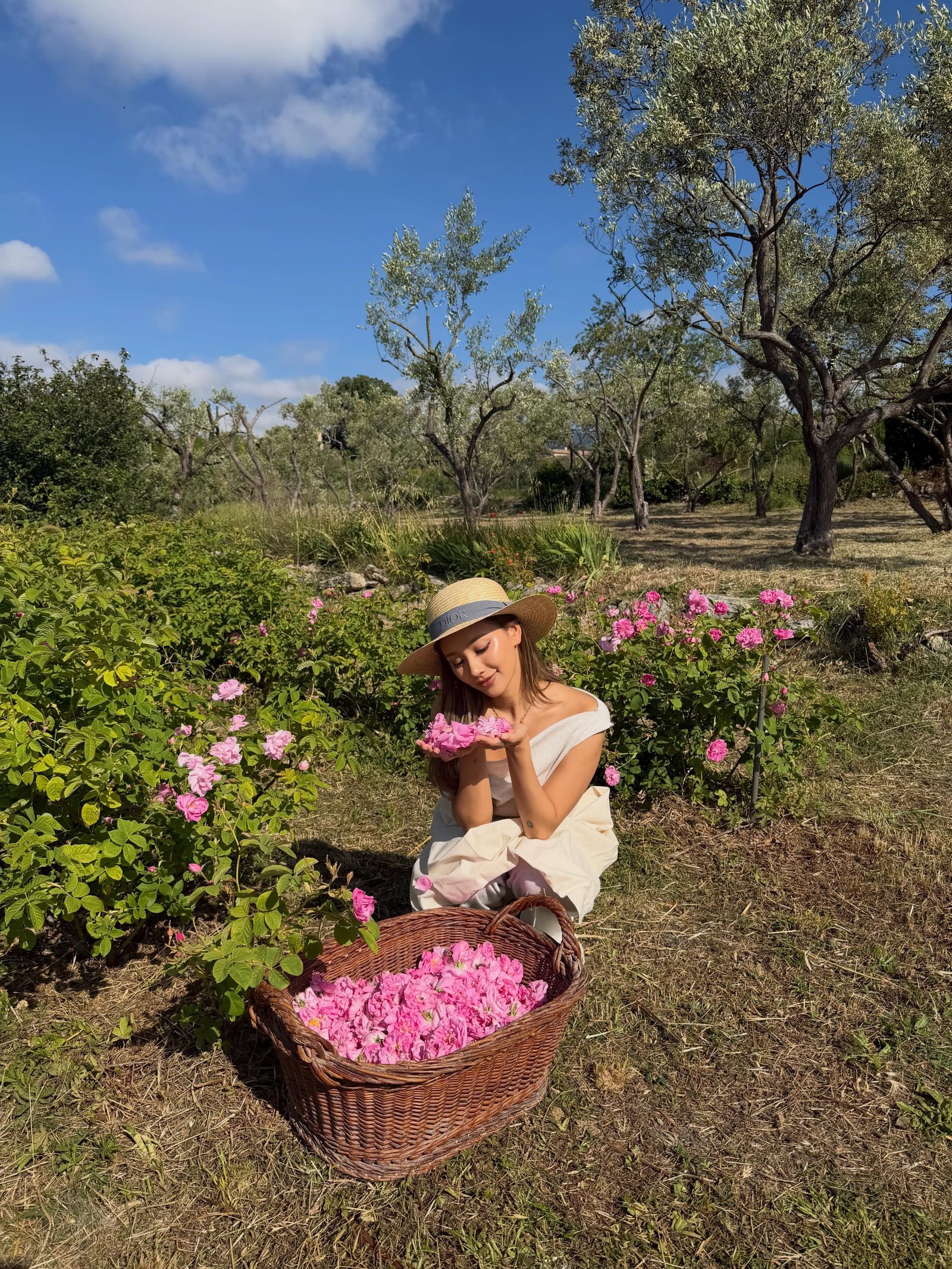 Kathy Zheng in a straw hat holding rose petals beside a basket of roses