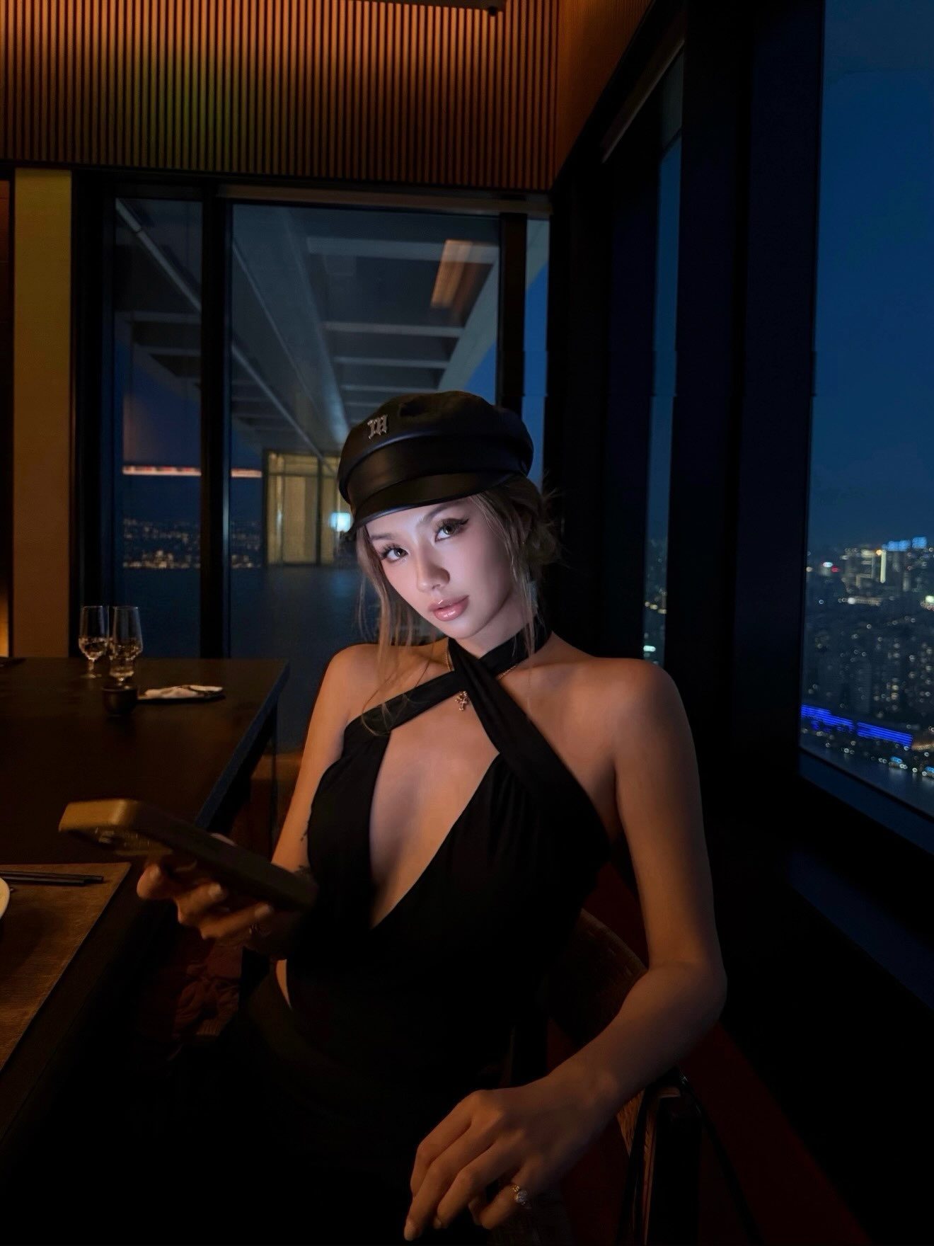 Kathy Zheng in a black halter and cap above a city at night