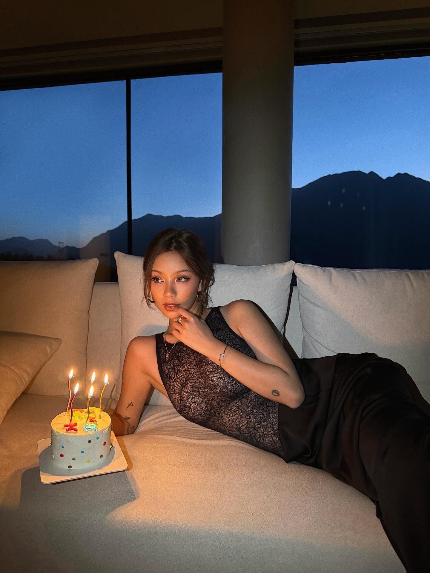Kathy Zheng in black lace beside a candlelit birthday cake at blue hour